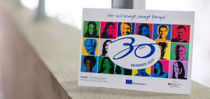 Eine Postkarte der NA DAAD mit dem "30 Jahre Erasmus Logo"  und Informationen zum Erasmus Programm steht auf einer Mauer.