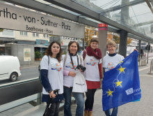 Mitarbeiterinnen der Nationalen Agenturen in ErasmusDays-T-Shirts warten mit Europa Fahne und  an der Haltestelle auf die Erasmus+ Bahn