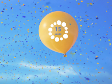 Luftballon in Orange mit Aufdruck 15 Jahre vor blauem Himmer mit buntem Konfetti in der Luft