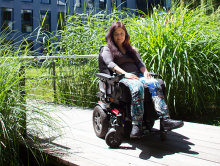 Die Studierende ist in ihrem Rollstuhl in der Sonne vor der Hochschule zu sehen.