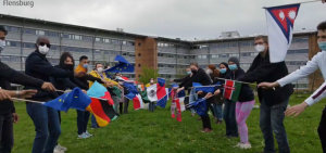 Studierende tanzen mit kleinen Flaggen für die Choreographie zur Jerusalema-Challenge auf den Grünflächen der Uni