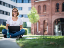 Eine Mitarbeiterin des International Office sitzt draußen an der Hochschule und informiert sich online über die Unterstützung und Expertise der NA DAAD bei der Umsetzung des Erasmus+ Programms.