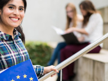 Eine Studentin lächelt in die Kamera und hält Informationsmaterial der NA DAAD über die Strategie Europa 2020 in der Hand.