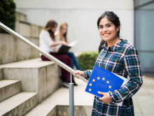 Eine Studentin hält Informationsmaterial der NA DAAD mit einer aufgedruckten europäischen Flagge im Arm. Zwei Studierende informieren sich über die Erasmus+ Partnerländer.
