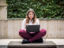 Eine Studentin arbeitet mit Headset im Schneidersitz an ihrem Laptop