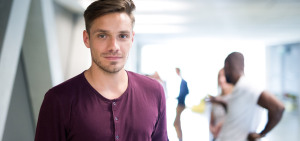 Ein Erasmus-Student steht in einer Hochschule und blickt in die Kamera. 