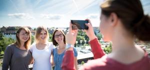 Eine Studentin fotografiert drei Kommolitoninnen mit einem Smartphone