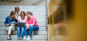 Studierende sitzen auf Treppen Ihrer Hochschule und tauschen sich vor einem Laptop über Vorteile der Strategischen Partnerschaften aus.
