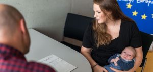 Eine Studentin sitzt mit ihrem Baby im Arm im International Office ihrer Hochschule und informiert sich über die Erasmus+ Möglichkeiten eines Auslandsaufenthalts mit Kind 