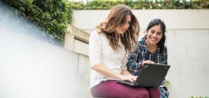 Zwei Studentinnen sitzen draußen und lesen auf einem Laptop den Erasmus+ Blog