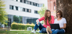 Zwei Alumni lesen einen Erasmus+ Bericht auf einem Laptop im Freien.
