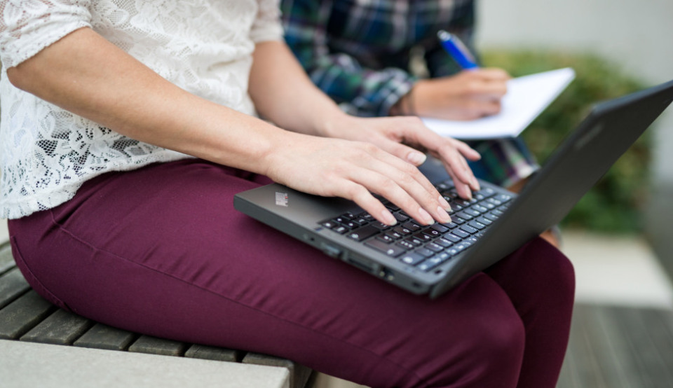 Eine Studierende registriert sich vor ihrer Hochschule an ihrem Laptop als Antragsstellerin.