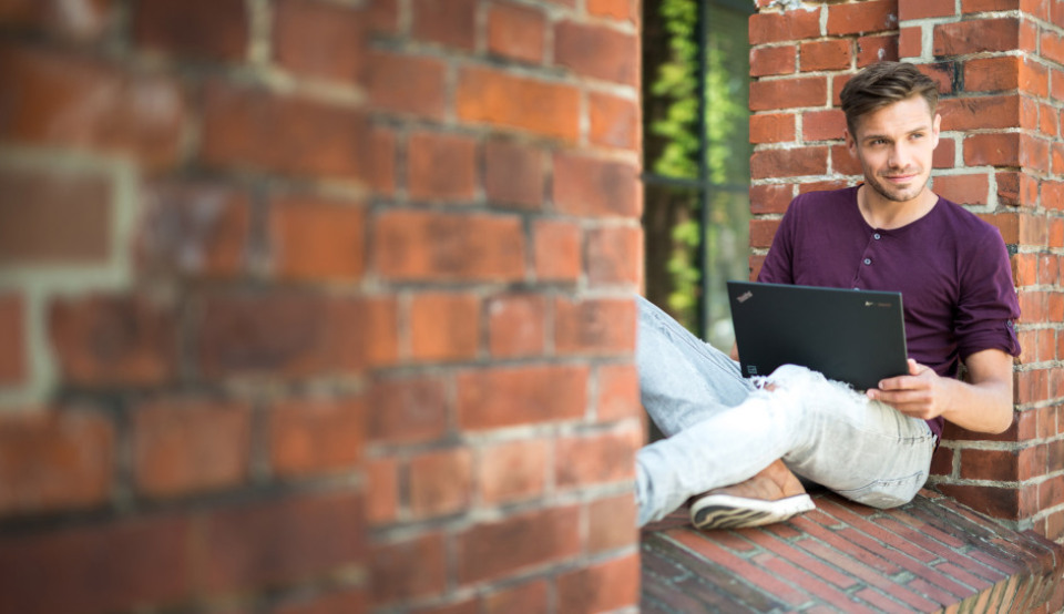 Ein Student sitzt draußen an seiner Hochschule und informiert sich online über ein Auslandspraktikum mit Erasmus+.