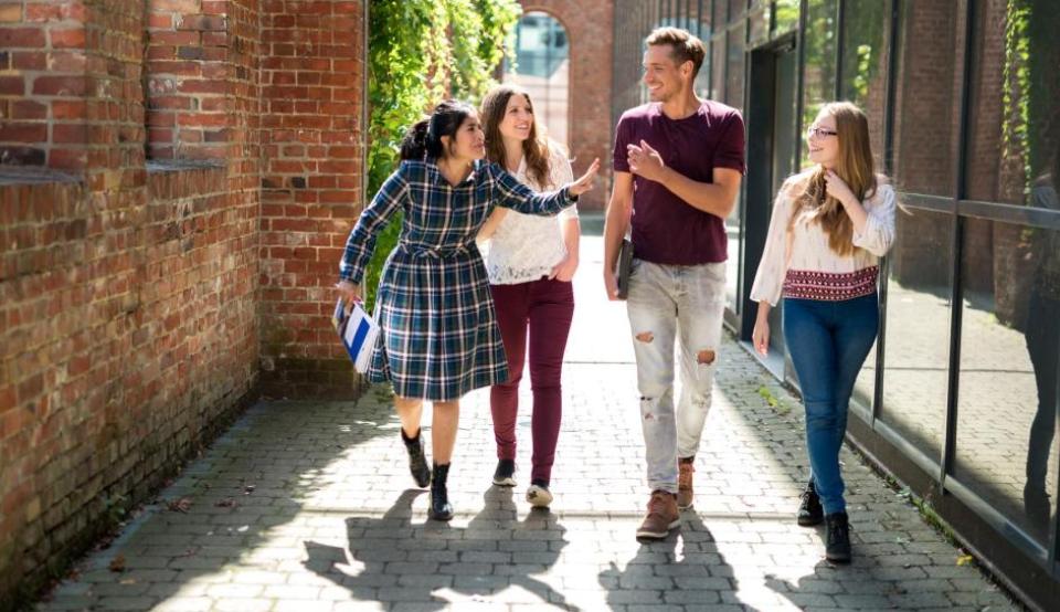 Vier Erasmus+ Studierende laufen über ihren Hochschulcampus und unterhalten sich über ihr Projekt im Rahmen von Europa macht Schule.