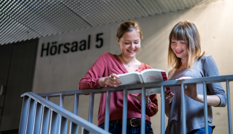Zwei Studentinnen informieren sich vor einem Hörsaal über die Erasmus+ Masterdarlehen.